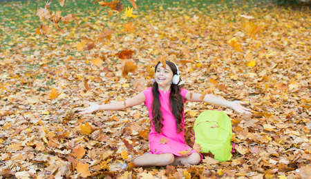 happy child throw up autumn leaves while listen music in headphones, childhood