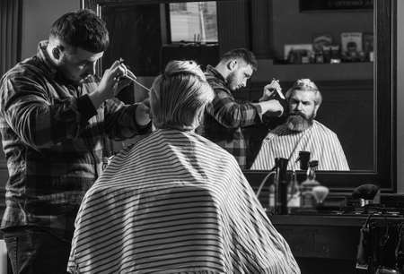 Fashion portrait of man. Barbershop. Young hipster man with beard cutting his hair in a barbershop. Professional hairdressing work. Lifestyle. master barber does the hairstyle and styling with dryerの写真素材