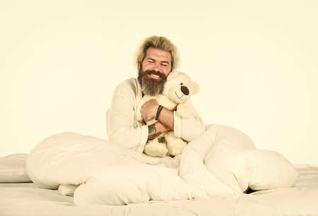 Lovely hipster. Create sleep positive bedroom environment. Playful adult. Cute and romantic. Bearded hipster play toy. Man hug soft toy relaxing in bed. Make surprise concept. Cute teddy bear toyの写真素材