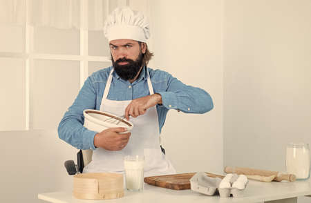 Time for good food. male cook preparing food in home kitchen. brutal hipster in apron cooking meal. time for eating. serious baking. concept of housekeeping. mature bearded man wear chef hatの写真素材