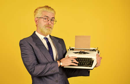 Salesman vintage objects. Mature man dyed beard hair yellow background. Used goods store. Connoisseur of vintage values. Vintage typewriter. Writer stick old habits. Businessman use retro technologyの写真素材