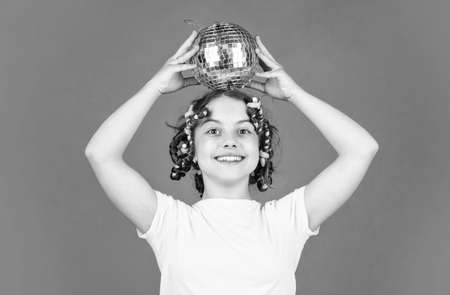 Retro party. Child hold golden disco ball. Cheerful girl with disco ball. Fashion kid posing with curlers in hair. Fancy teen. Hairstyle for disco party. Have fun. Night club. Hairdresser salonの写真素材
