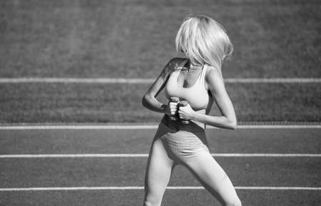 female athlete do weightlifting sport workout. trainer or coach training with dumbbell. perfect body shape. healthy and sporty. sexy fitness woman in sportswear. athletic lady use barbells on stadiumの写真素材