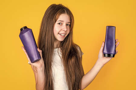 look here. child use shampoo in bottle. hair conditioner. beauty. wash and rinse. happy teen girl presenting cosmetic product. shampooing hair in salon. daily habits and personal careの写真素材