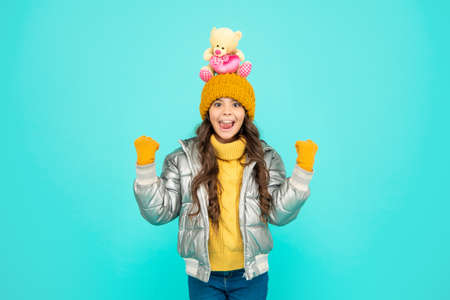 surprised teen girl in winter clothes hold toy on blue background, gift