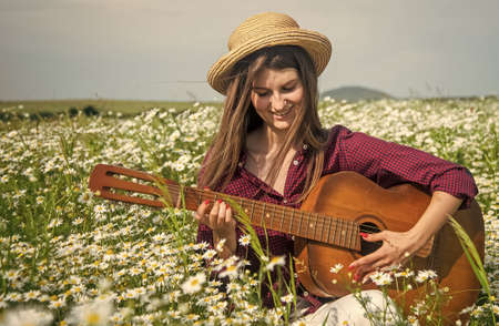 happy woman gather flowers in summer daisy field play acoustic guitar, countryside