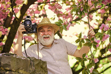 Senior man hold professional camera. Retirement travel. Enjoying free time. Travel and tourism. Capturing beauty. Happy grandfather. Spring holidays. Travel photo. Photographer in blooming gardenの写真素材