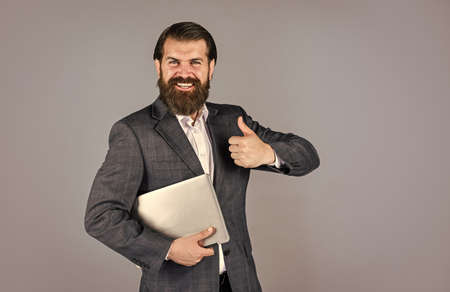 showing thumb up. brutal male with beard in suit. handsome ceo hold computer. boss and employee....