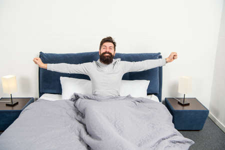 Happy guy smiling and stretching in bed waking up after sleep, morning