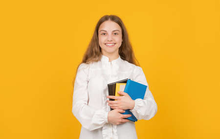 cheerful teen girl hold school workbook on yellow background, knowleldge