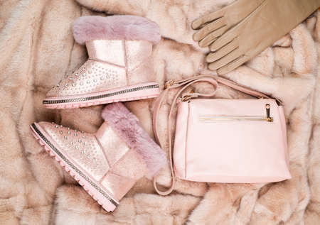 pair of fashionable winter ugg boots leather gloves and bag on fur background, fashion accessory