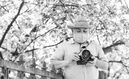 professional photographer work during coronavirus quarantine. man tourist use camera take photo of cherry blossom. sakura in full bloom photography. senior bearded man in respirator mask. Hot dayの写真素材