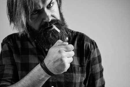 smoke a cigarette. bearded man. mature hipster with beard use a lighter. brutal caucasian hipster with moustache smoking cigarette. male bad habit. confident guy in checkered shirtの写真素材