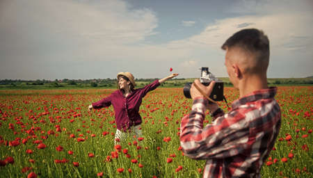 Being together. happy man and woman in love enjoy spring weather. happy relations. girl and guy in field with camera. romantic couple photographing in red poppy flowers. family summer vacationの写真素材