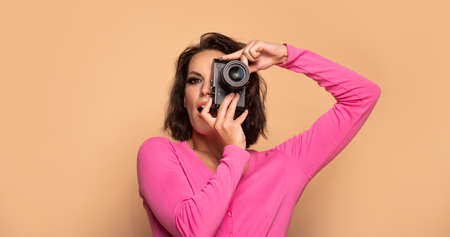 Portrait of serious girl photographer looking in photo camera beige background, photographingの写真素材