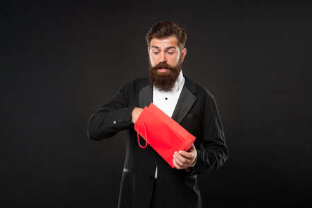 surprised curious man in tuxedo bow tie on black background with shopping bag for mens day.の写真素材
