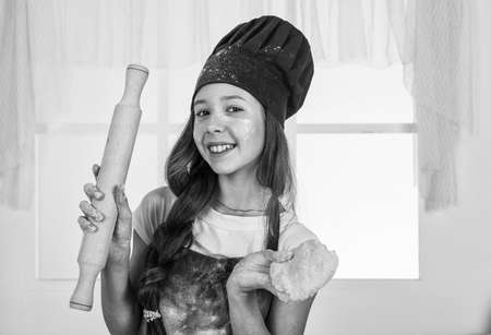 little helper roll the dough with rolling pin. culinary and cuisine. happy childhood. happy child wear cook uniform. chef girl in hat and apron. kid cooking food in kitchen. choosing a careerの写真素材