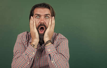 surprised mature bearded man teacher in school classroom with blackboard, surpriseの写真素材