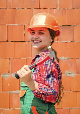 Repair concept. kid wear helmet on construction site. teen girl builder with building tool hammer. child on repairing work. concept of renovation in workshop. busy professional carpenterの写真素材