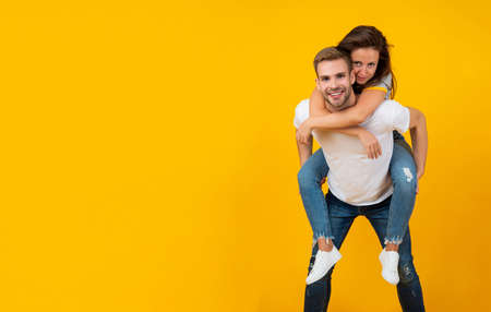 Happy romantic couple having fun doing piggyback ride yellow background copy space, loveの写真素材