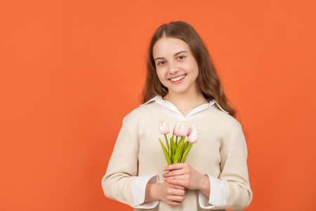 smiling teen girl with bouquet on orange background. childhood happiness.の写真素材