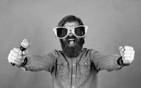 good day. male sing music in microphone. funny bearded man with mic. brutal caucasian hipster in party glasses. karaoke singer. unshaven guy with groomed long hairの写真素材