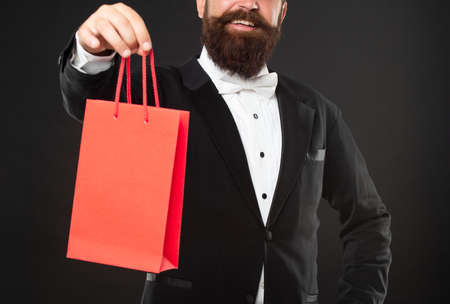 cropped smiling man in tuxedo bow tie presenting shopping bag. birthday. copy space.の写真素材