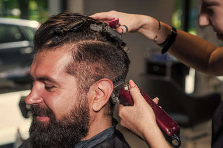 shaving with fun. hipster. male barber care. bearded man at hairdresser chair in salon. beauty and fashion. hair and beard styling. brutal guy with barbershop professional master use electric shaverの写真素材