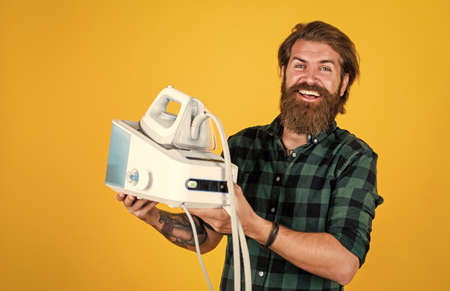 male housekeeper customer. happy shop assistant in checkered shirt. bearded man. new technology. mature hipster with beard use steaming iron. brutal caucasian hipster with moustache ironingの写真素材