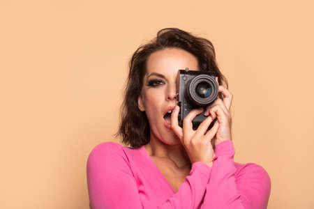 Portrait of excited girl photographer photographing with photo camera beige background, photographyの写真素材