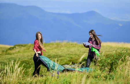 Summer mood. family camping. reach destination place. hiking outdoor adventure. mountain tourism camp. two girls pitch tent. wanderlust discovery. friends spend free time togetherの写真素材