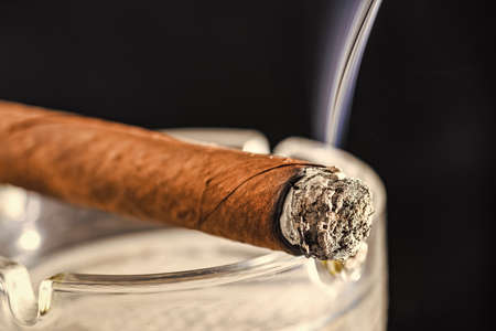 Lighting cuban cigar dark background. Tobacco smoking. Tobacco smoke. Nicotine addiction. Steaming...