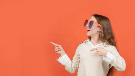 Happy child in big funny glasses pointing fingers aside brown background, copy spaceの写真素材