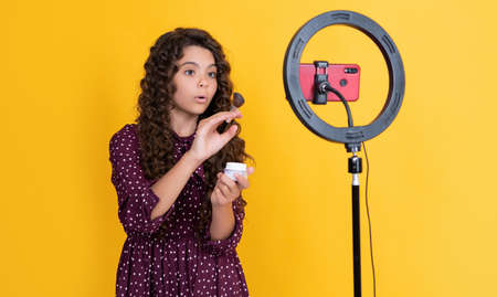 shocked child blogger with long curly hair making video for blog hold powder brush