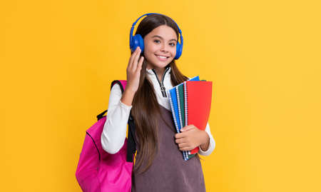 child smile in headphones with school backpack with workbook on yellow background