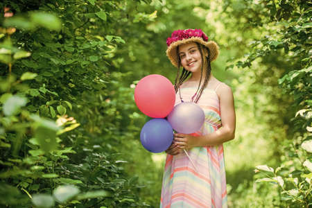 happy teen girl in straw hat with rose flowers in summer nature hold party balloons, childhoodの写真素材