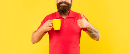 Happy bearded man crop view in casual red tshirt giving thumb holding mug, tea