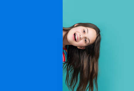 positive kid behind blank blue paper with copy space for advertisement