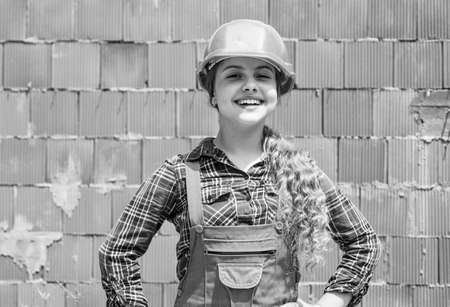 kid wear helmet on construction site. teen girl builder in building uniform. child on repairing work. concept of renovation in workshop. busy professional carpenterの写真素材