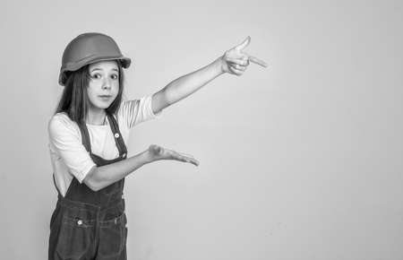 This will be perfect. kid builder on construction site. worker engineer. architect in workshop. renovation and repair. pointing finger on copy space. teen girl in boilersuit. child wear hard hatの写真素材