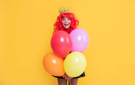 glad child in crown with party balloon on yellow backgroundの写真素材