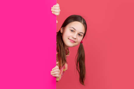 cheerful girl behind blank pink paper with copy space for advertisement