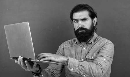 serious mature teacher working on computer. brutal bearded man work in classroom with laptop. online prepare for exam. college lecturer on private lesson. back to school. online informal educationの写真素材