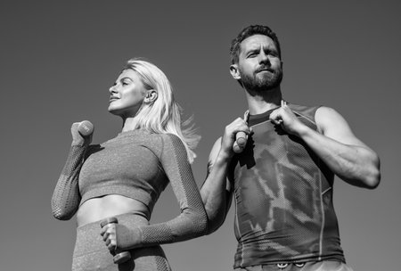 sport couple in sportswear training with barbells and skipping rope on sky background, fitness