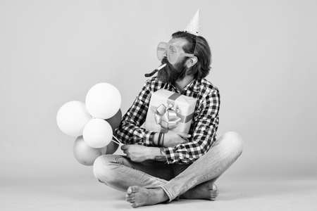 anniversary. have a happy holiday. party time. happy birthday to you. bearded mature man celebrate birthday party. cheerful man in bday hat hold holiday balloons. gifts and presents conceptの写真素材