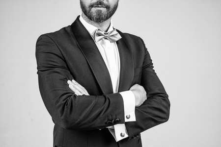 Confident bridegroom with unshaven beard cropped view wear elegant fashion tuxedo with bow tie keeping arms crossed grey background, confidenceの写真素材