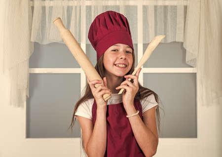 kid chef cooking with rolling pin and wooden spoon. child prepare healthy food at home and wearing...