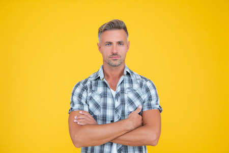 mature man with grizzle hair on yellow background. crossed handsの写真素材