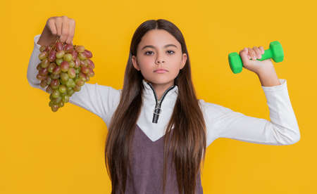 serious child hold fresh grapes and sport barbells on yellow backgroundの写真素材
