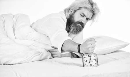Hate early morning awakening. Sleepy guy and alarm clock in bed. Bearded man with alarm clock. Hipster want to sleep. Schedule. Getting to bed on time. Get up right now. Stressed man alarm clockの写真素材